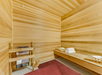 Wooden sauna room with a bench and a stack of towels. A heater is placed on the left side, and a red mat covers part of the floor.
