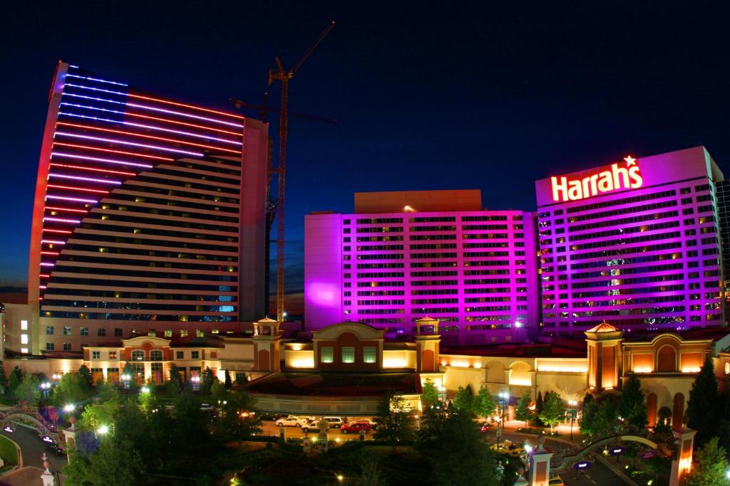 Night view of a brightly lit casino complex with a prominent "Harrah's" sign and a high-rise building with colorful lights.