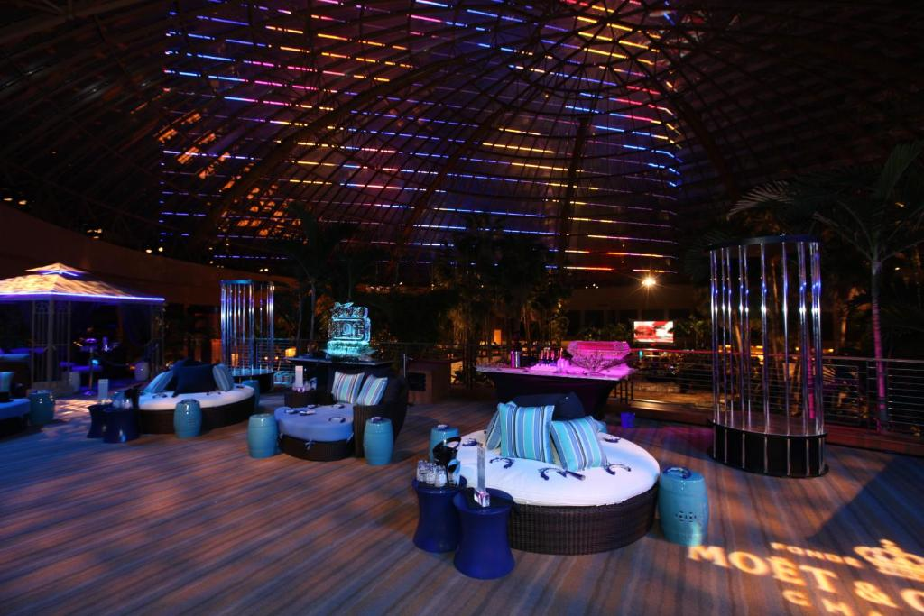 A dimly lit lounge with round seating, striped cushions, and colorful overhead lighting.