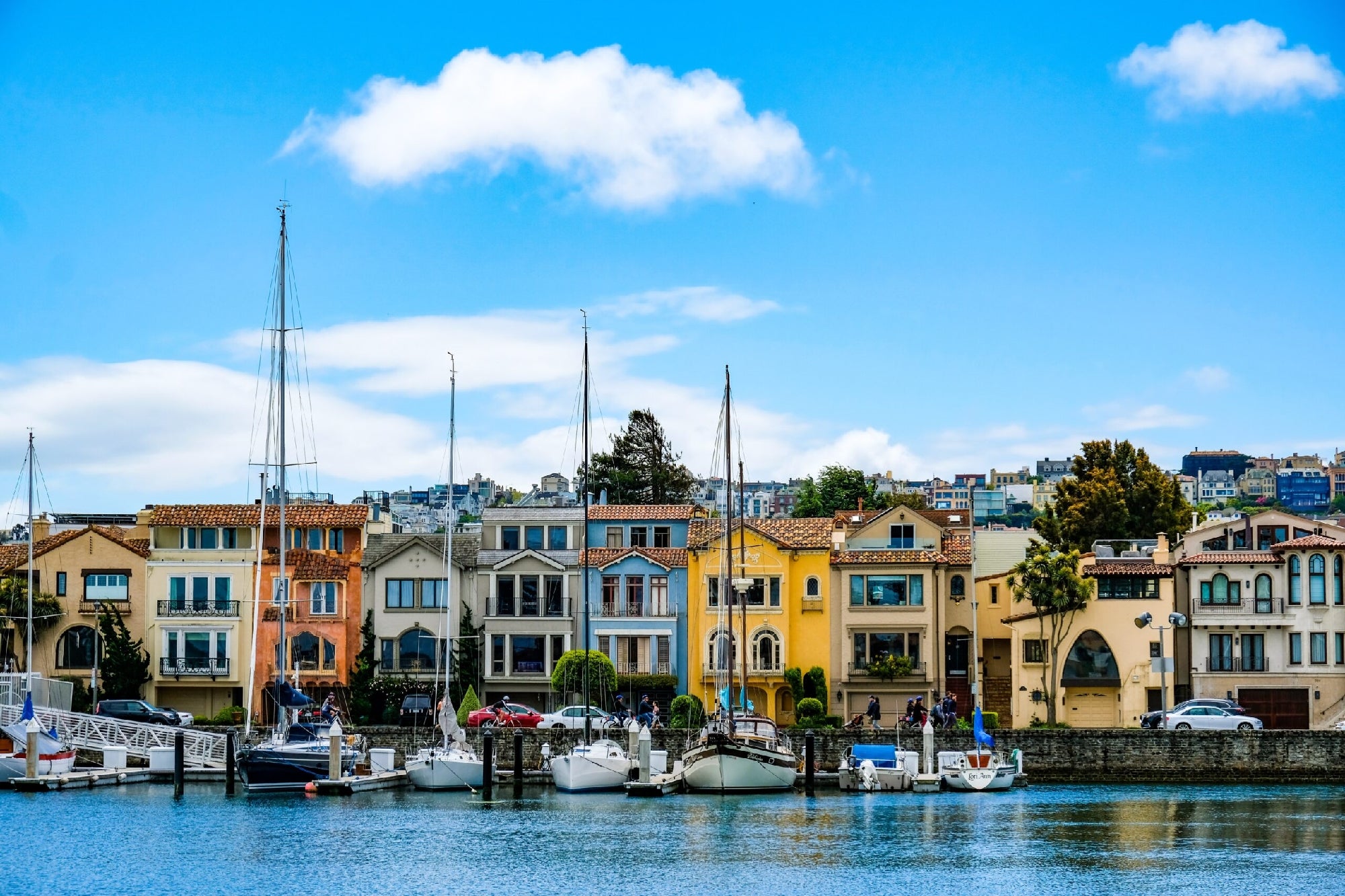 A row of colorful houses by a waterfront with several moored boats. Blue sky with scattered clouds above.