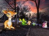 Large illuminated animal and plant lanterns, including a deer, bunny, and snail, are displayed outdoors at sunset with bare trees and a stone building in the background.