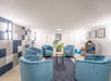 Room with four blue chairs around a small round table, a dark rug, tiled walls, a plant, and a shelf with toys.