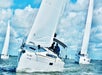 Three sailboats with white sails are sailing on open water under a blue sky with scattered clouds.