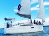 A group of people sail a white Sun Odyssey 349 yacht with a pirate flag on a sunny day, with blue sky and water in the background.