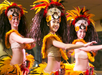 Three dancers in vibrant, feathered costumes and headdresses perform a traditional routine.