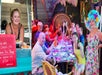 A smiling woman serves food from a cart. Nearby, a colorful group of people enjoys a meal and drinks around a vibrant, tiki-themed table.
