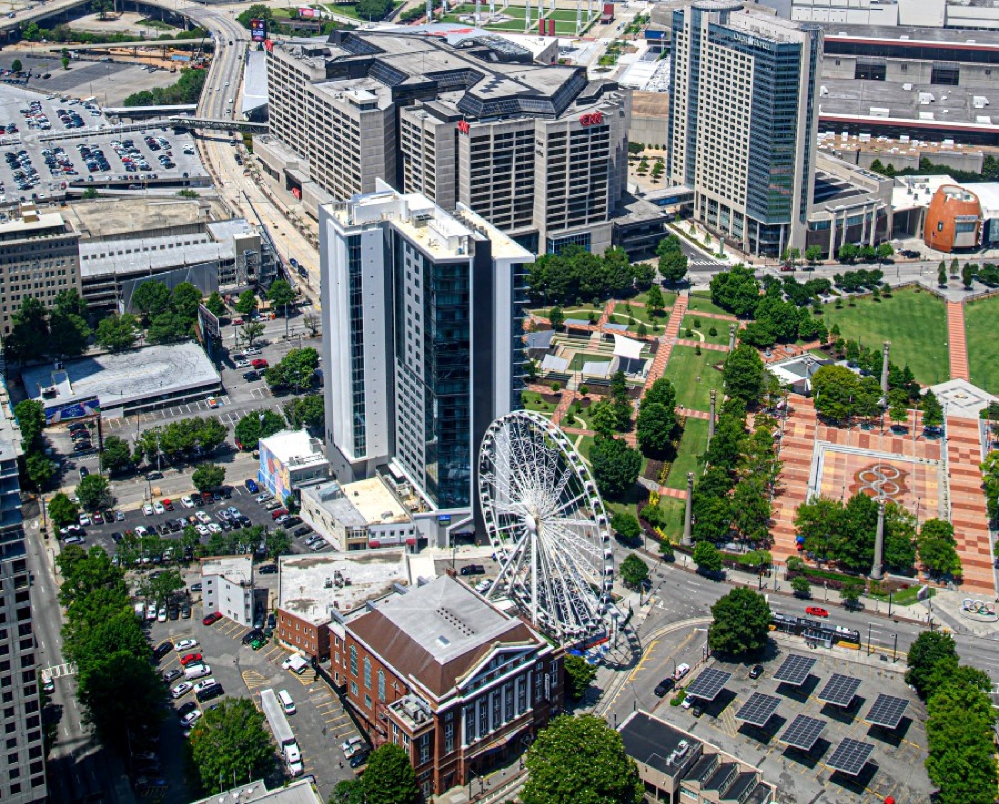 Aerial view of downtown Atlanta featuring a Ferris wheel, modern buildings, parking lots, and a green public park area.