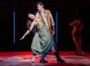 A man and a woman in costume perform a dramatic dance pose on stage, with a spotlight on them and another person in the background.