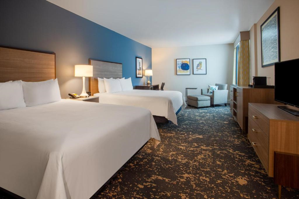 Two Queen beds, seating area, a desk and chair, and a flat-screen TV inside a guest room.