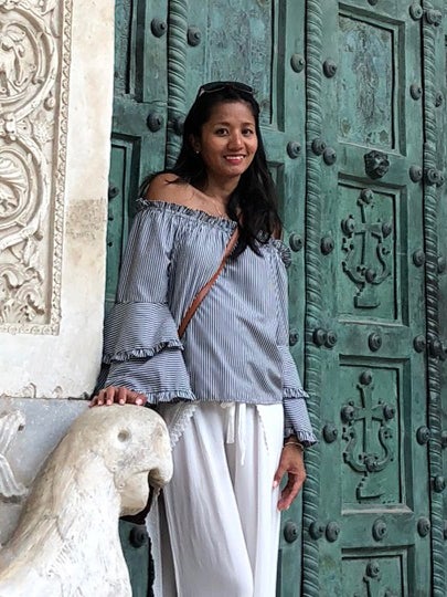 Rosemarie Rose, Director of Partner Success for Places to Stay at Tripster, standing by an ornate door in a stylish off-the-shoulder top and white pants.