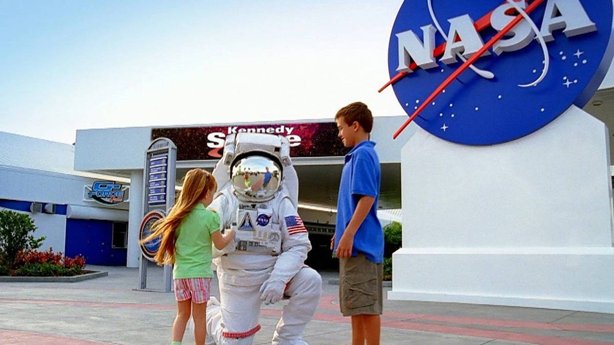 Children interacting with an astronaut at Kennedy Space Center in Orlando, Florida, with the NASA logo prominently displayed.