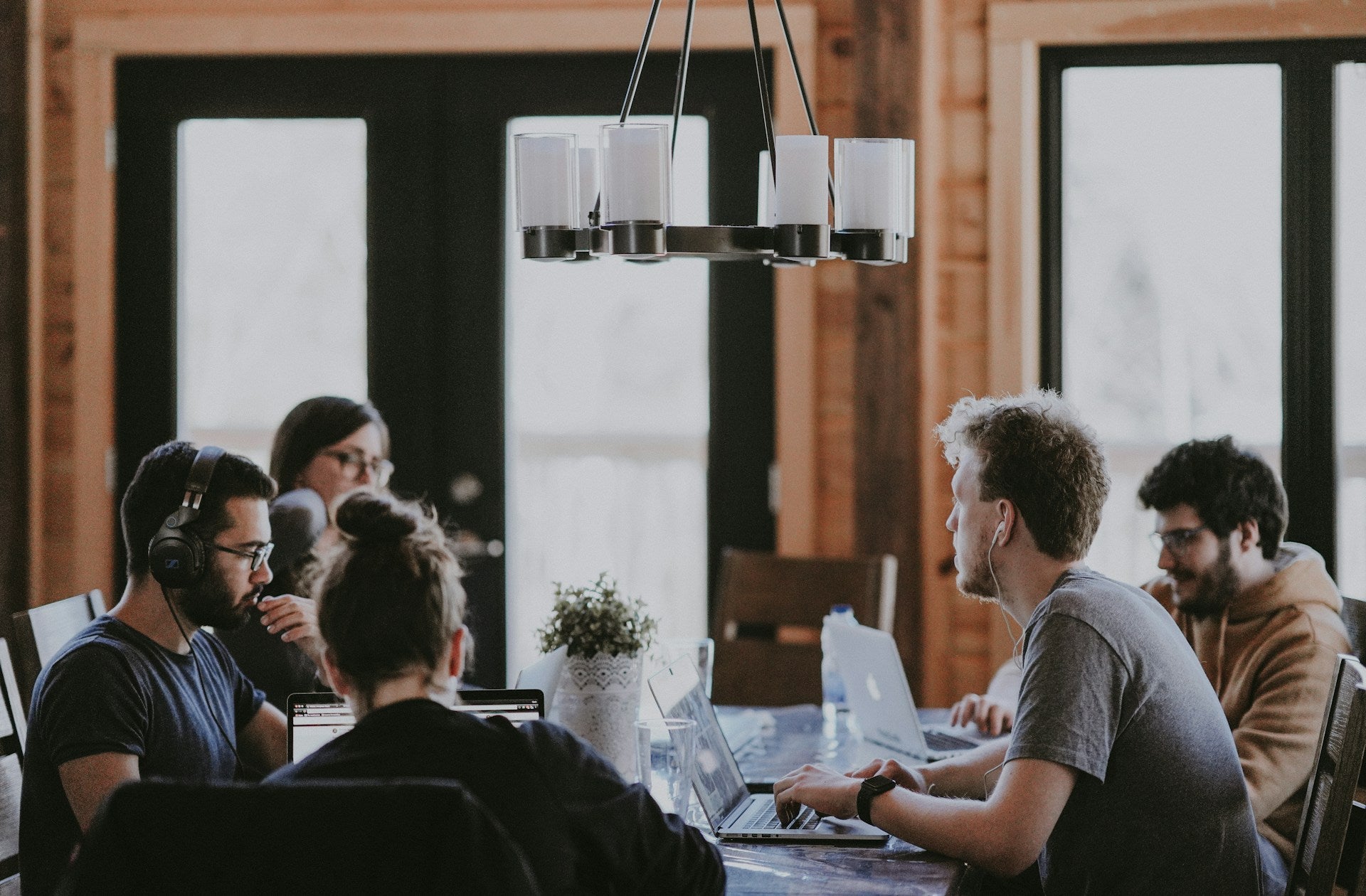 Group of young professionals collaborating on laptops in a modern, rustic workspace