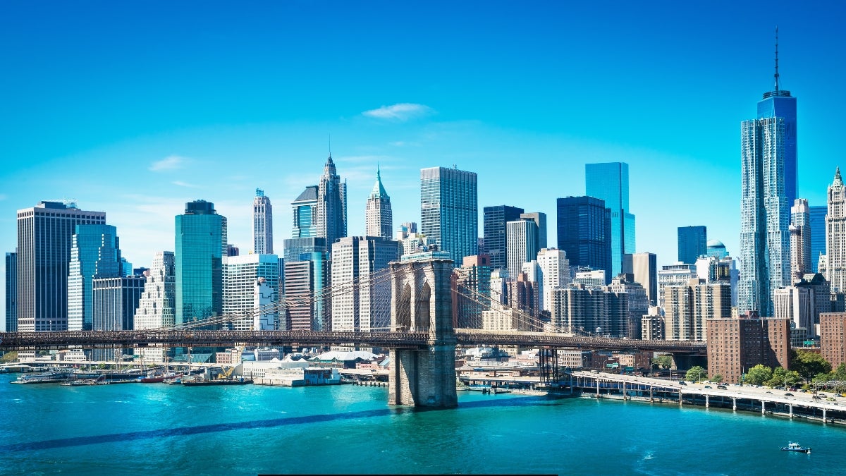 A panoramic view of the Brooklyn Bridge spanning across the East River with the New York City skyline in the background on a clear day.