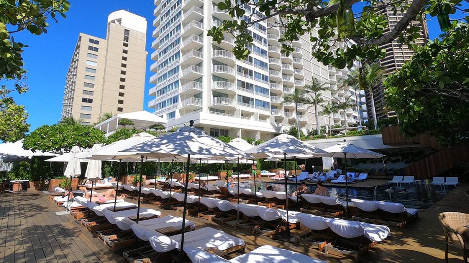 View of the pool and several chairs to layout on with umbrellas at The Modern Honolulu in Oahu, Hawaii, USA