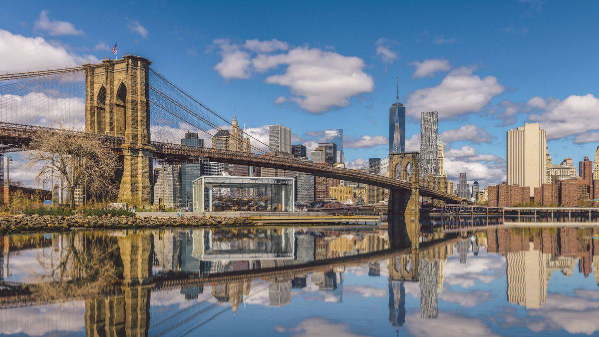 view of Brooklyn Bridge over water with skyline in background in NYC, New York, USA