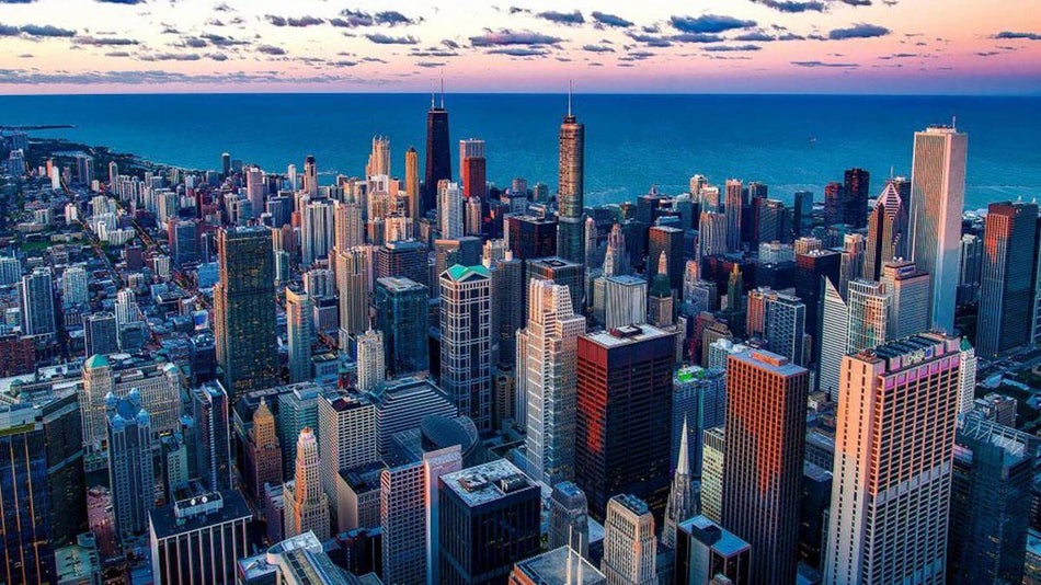 aerial view of chicago cityscape with view of water in distance and light pink sky