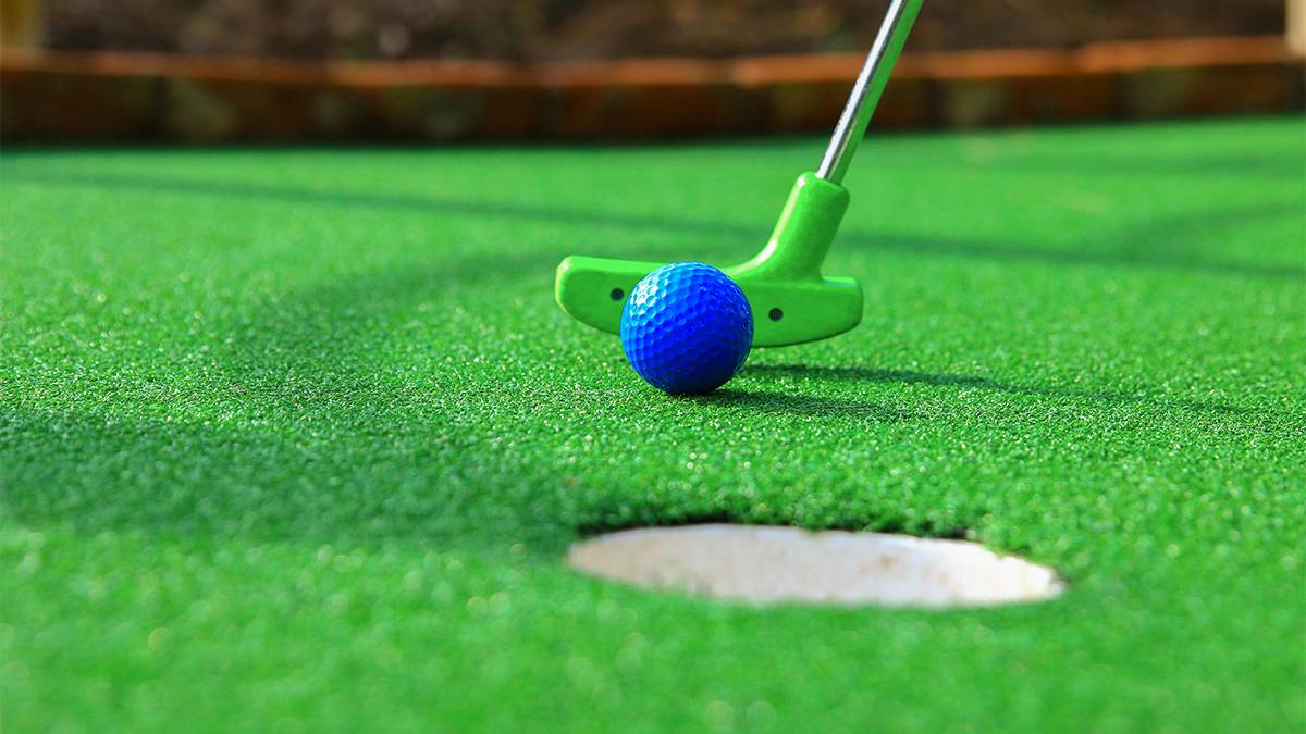 Close up of a green mini golf club and a blue ball near a hole.