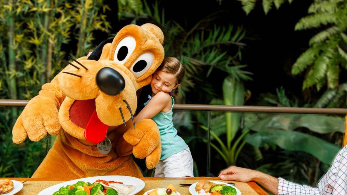 girl hugging Pluto character at dinner with food on table at Disneyland in Los Angeles, California, USA