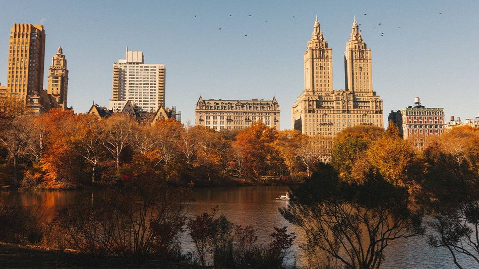 Wide shot looking out over water in Central Park with tall buildings in the background in NYC, New York, USA