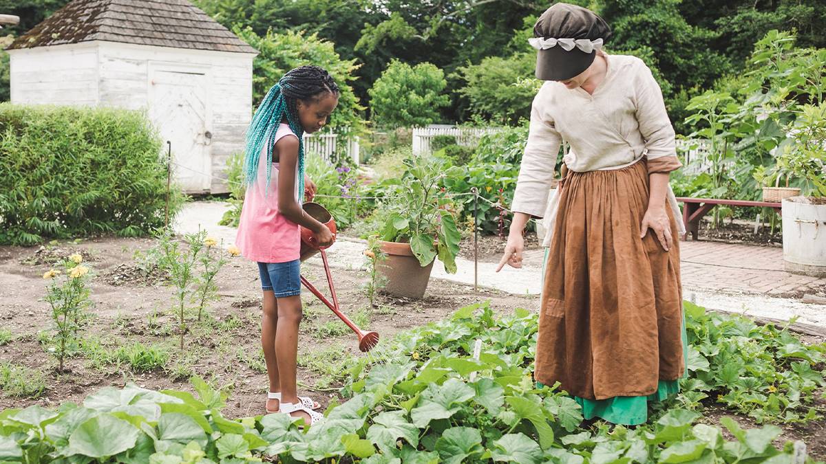 Young girl watering a garden with a cast member at Colonial Williamsburg - Williamsburg, Virginia, USA