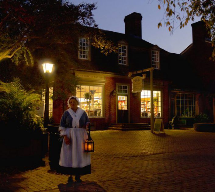 woman in costume holding lantern in front of store in Colonial Williamsburg, Virginia, USA