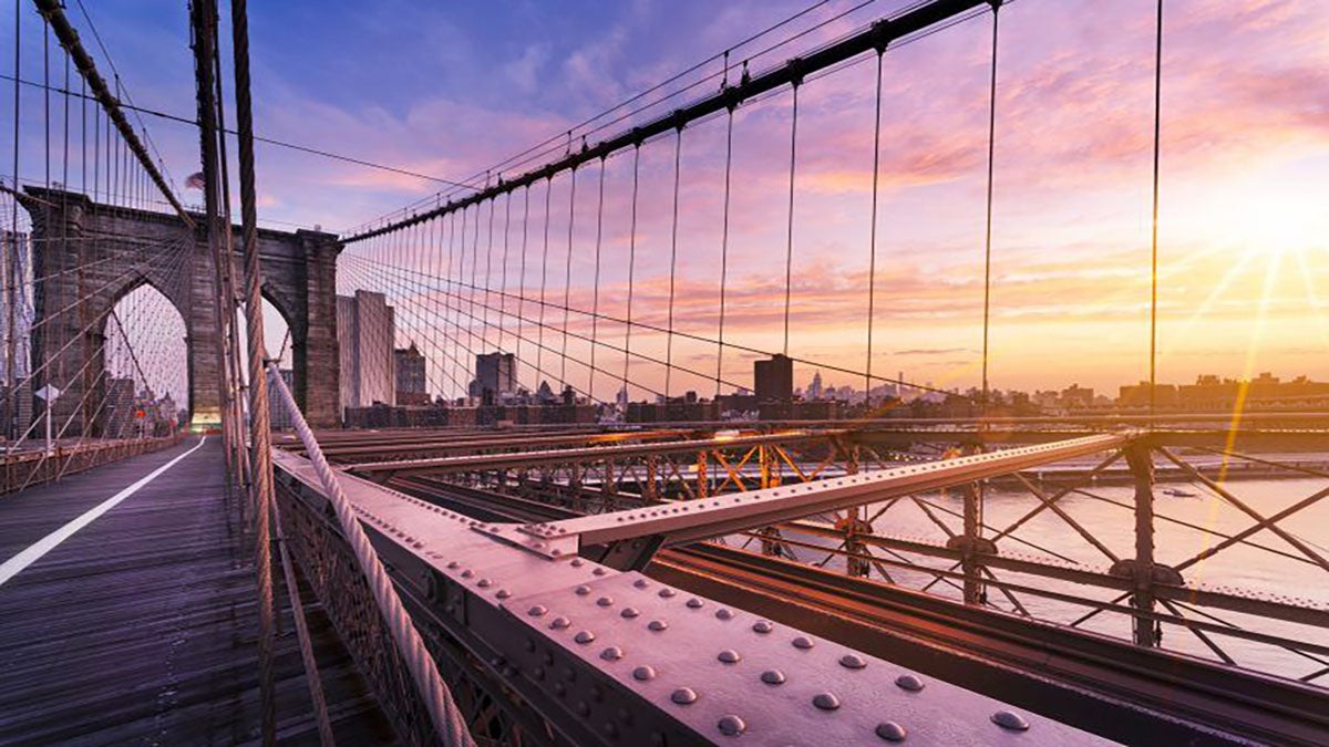 view from on the Brooklyn Bridge looking over the East River at sunset with city skyline in background in NYC, New York, USA
