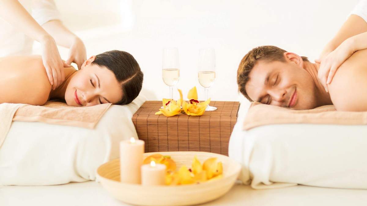 man and woman with champagne glasses and candles getting a couples massage