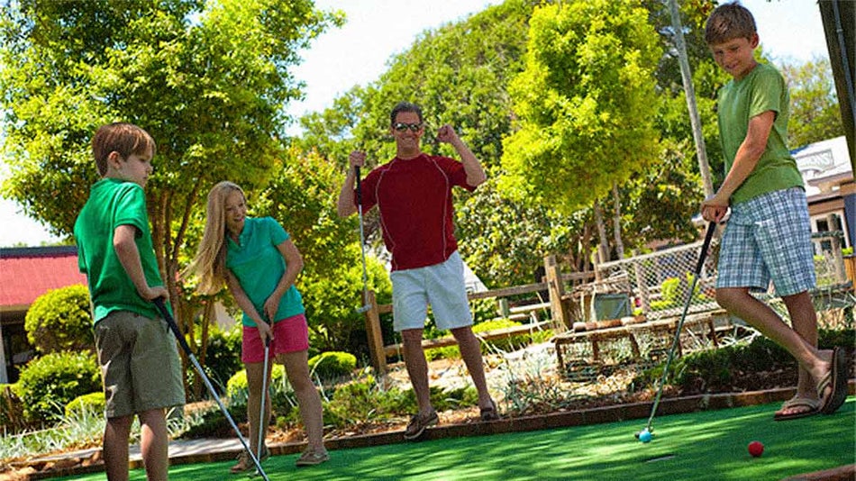 family of four in shorts and t shirts playing outdoor mini golf together