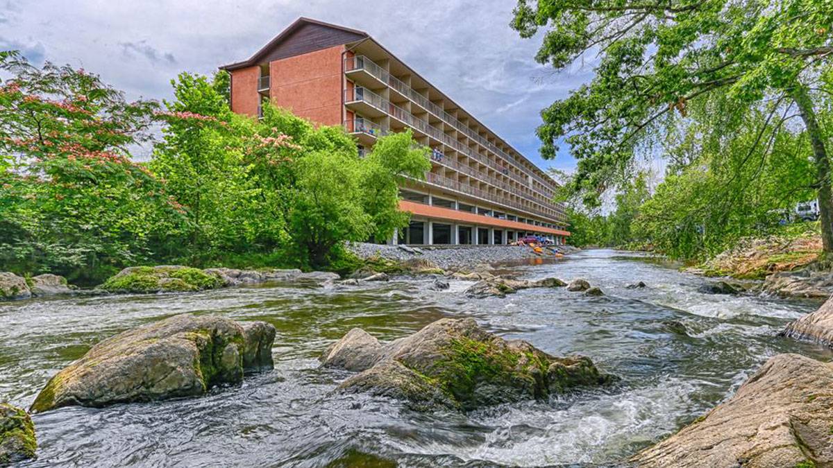 exterior of Creekstone Inn surrounded by trees with close up of flowing water and stones in Pigeon Forge, Tennessee, USA