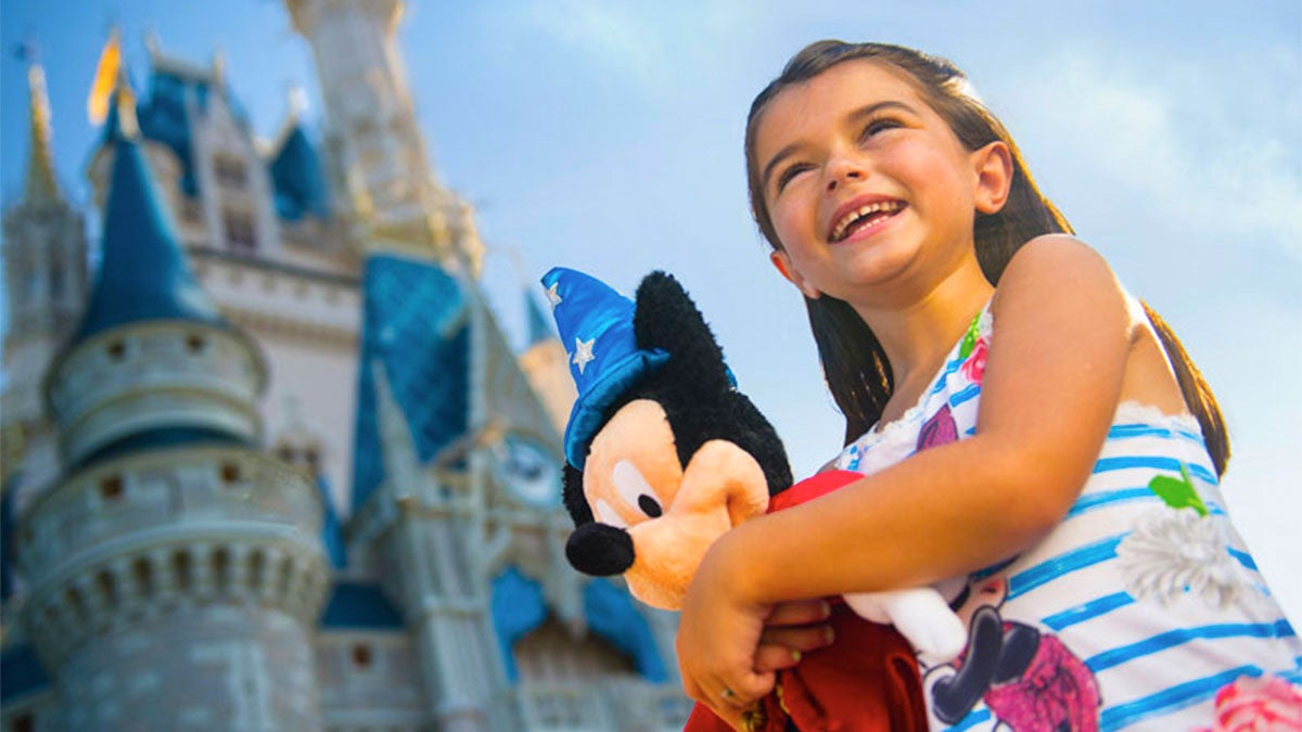 little girl holding mickey mouse toy standing in front of Cinderella castle at Walt Disney World in Orlando, Florida, USA