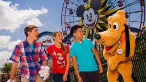 A group of teen agers laughing with Pluto and the Mickey Ferris wheel in the background at Disneyland in Los Angeles, California, USA
