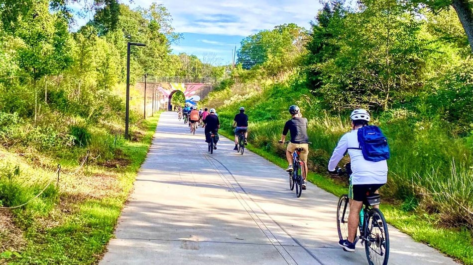 Ground view of people riding bikes towards a tunnel at BeltLine Arboretum on a sunny day in Atlanta, Georgia, USA