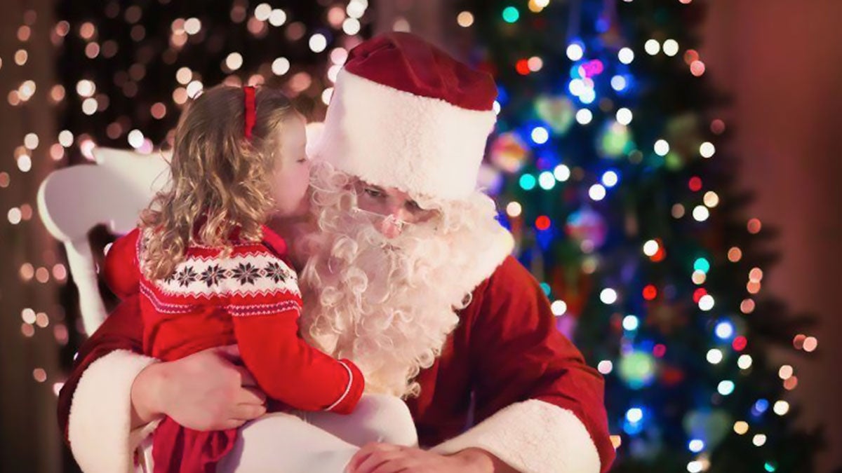 child whispering in santa's ear with christmas tree and lights in background