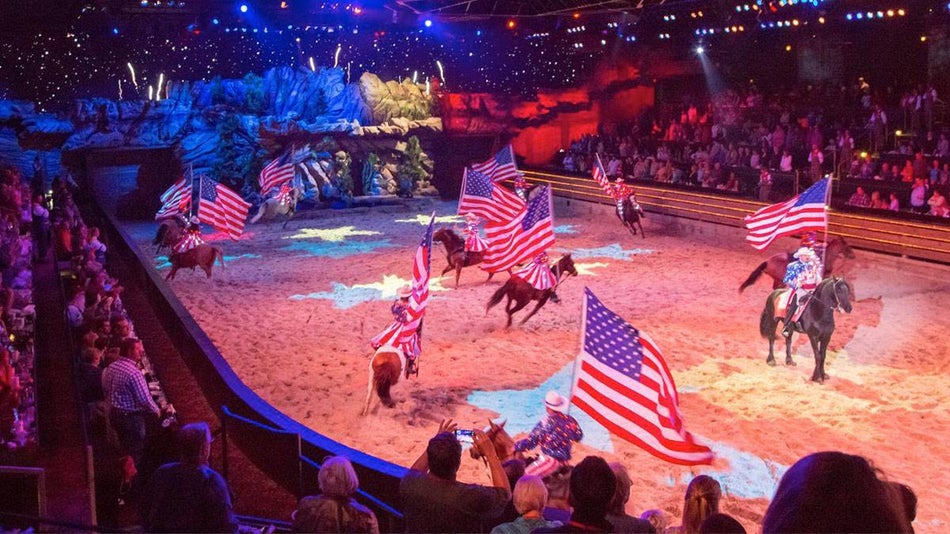 Dolly Parton's Dixie Stampede Riders on horses holding United States Flags with crowd watching in Branson, Missouri, USA
