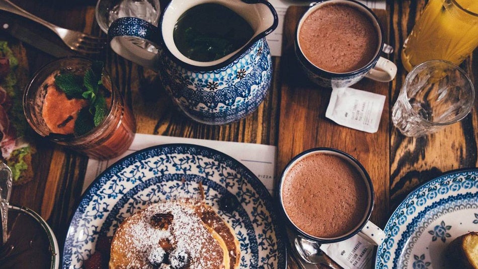 table with plates of pancakes and cups of hot chocolate