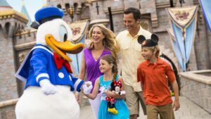 Family walking with Donald Duck in front of sleeping Beauty's Castle at Disneyland in Los Angeles, California, USA