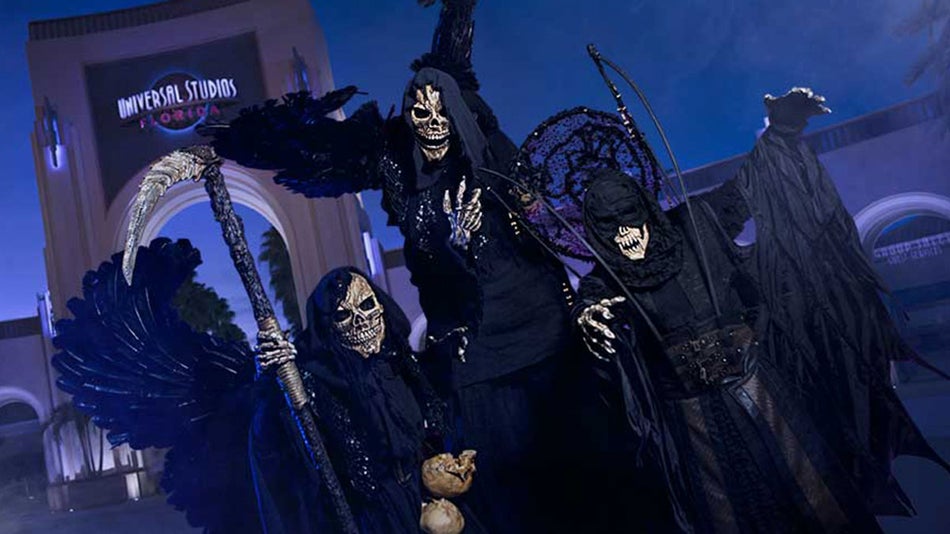three skeletons in dark scary costumes standing in front of entrance of Universal Studios during Halloween Horror Nights in Orlando, Florida, USA