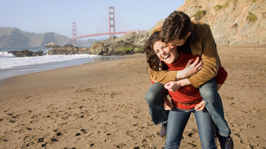 couple laughing together on beach in san francisco with golden gate bridge in the background