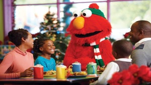 elmo greeting family sitting at table with multicolored hot chocolate mugs