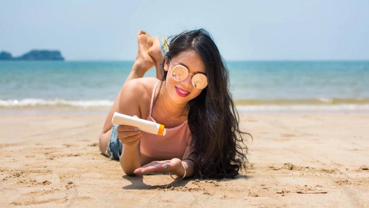 woman laying on beach with a bottle of sunscreen