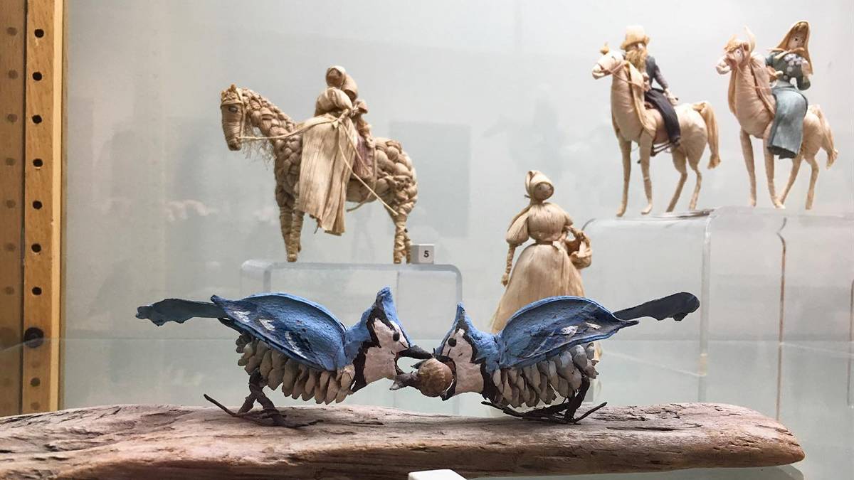 Close up photo of two bluejays made out of pines cones from 1960 fighting over a nut with other handmade figurines in the background at the Folk Art Center in Asheville, North Carolina, USA
