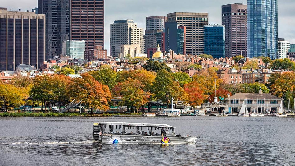 Duck tours boat on the water with the city and some trees in the background on a cloudy day in Boston, Massachusetts