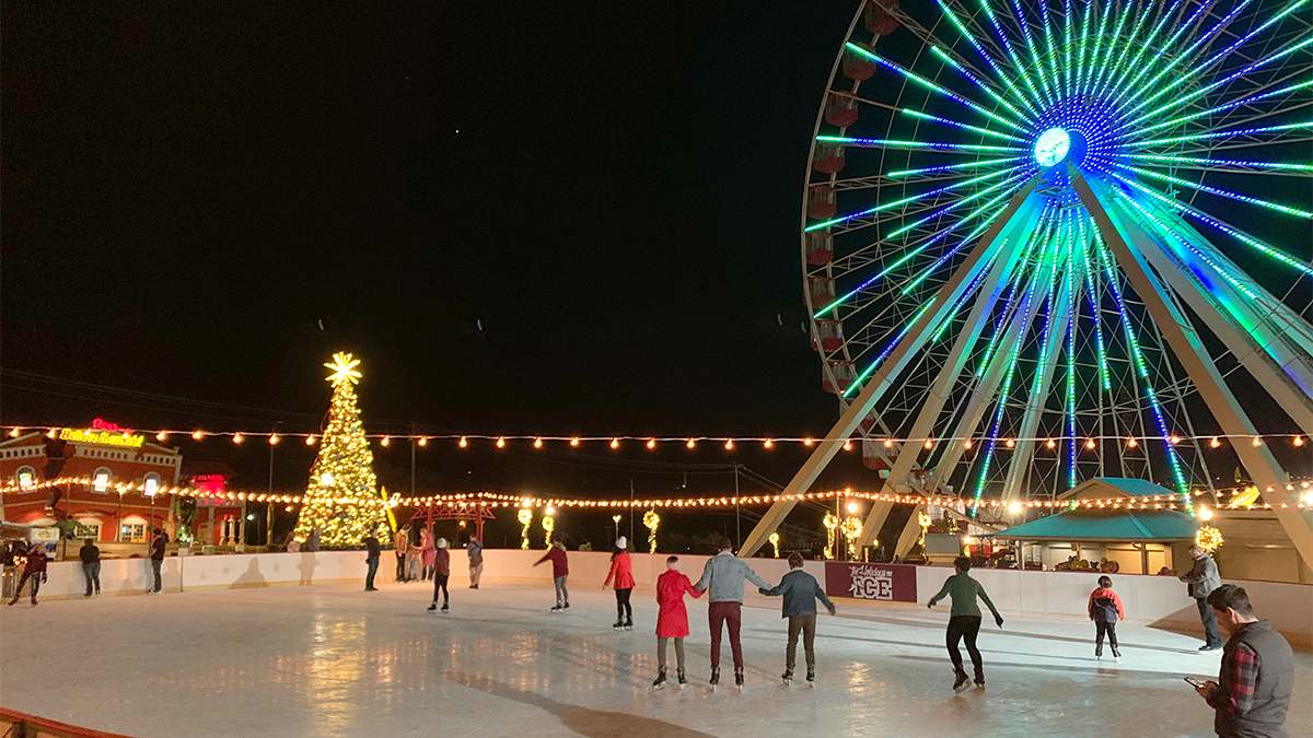 People ice skating and a large Ferris wheel with lights and a Christmas tree in the background in Branson, Missouri, USA