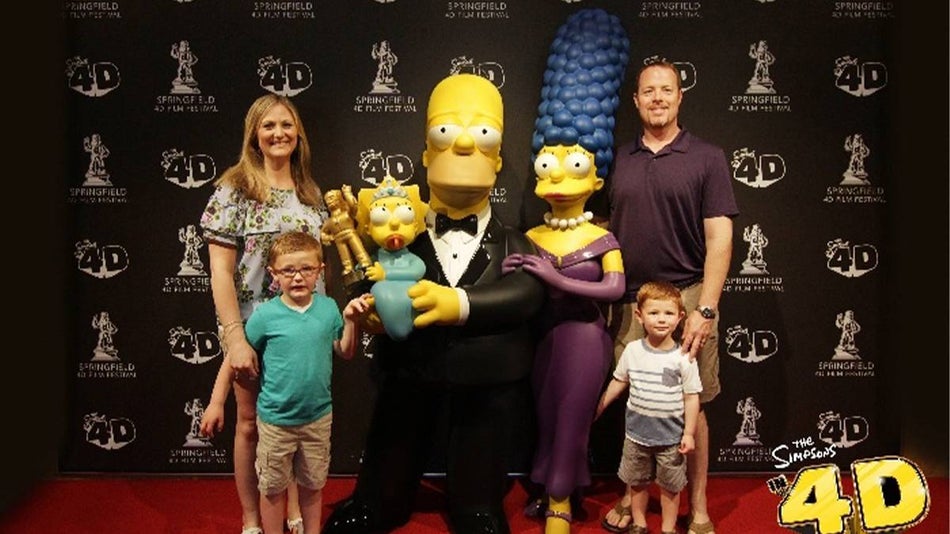 A family posing with statues of the Simpsons Family at The Simpsons 4D in Myrtle Beach, South Carolina