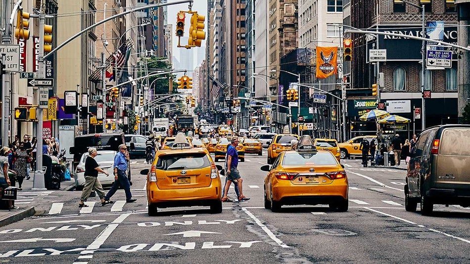 Wide shot of a busy NYC street with lots of people and taxis in New York