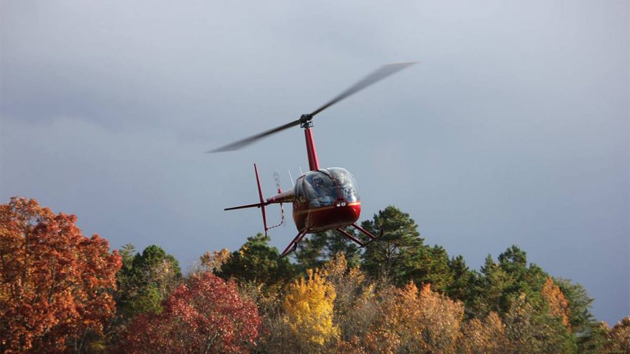 View of a red helicopter from Sevier County Choppers in the air over trees in the fall with a grey cloudy sky in Gatlinburg, Tennessee, USA