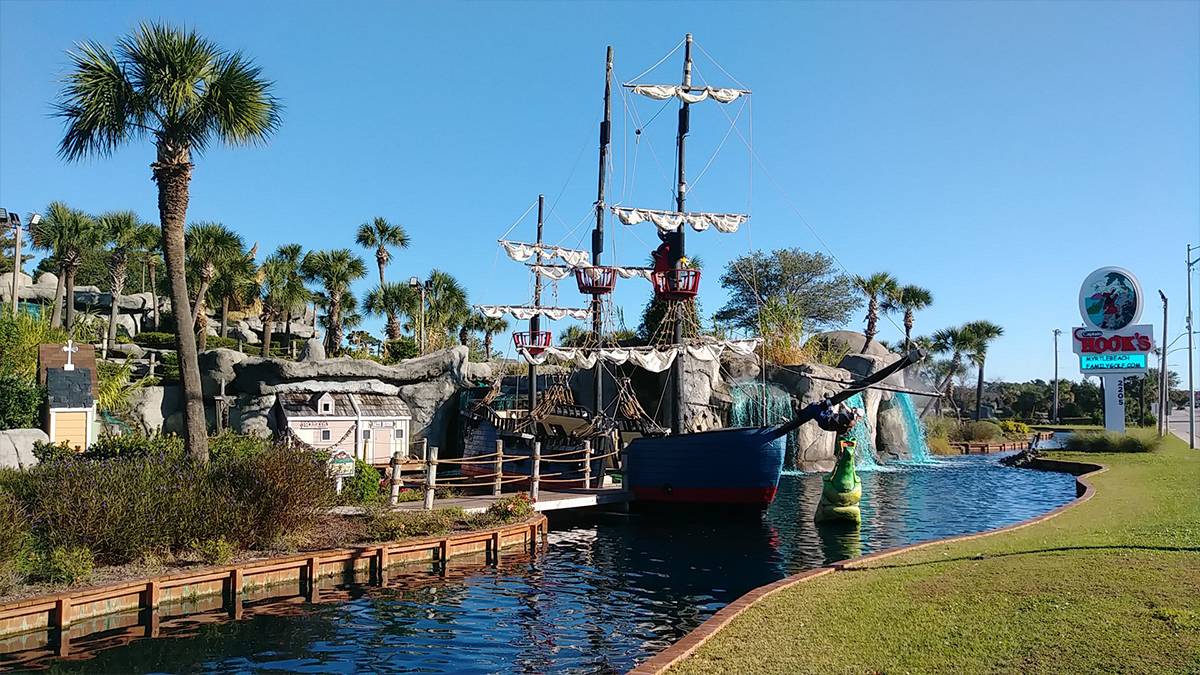 Wide shot of a pirate ship in the water and the mini gold course surrounding it at Captain Hook’s Adventure Golf in Myrtle Beach, South Carolina, USA
