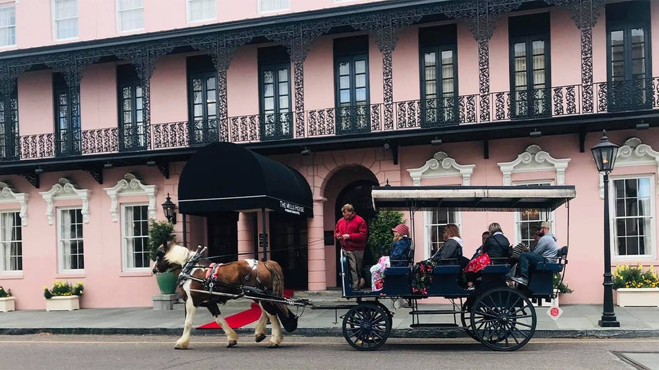 Side view of a group of people on a carriage ride of downtown Charleston with a pink building behind them in Myrtle Beach, South Carolina, USA