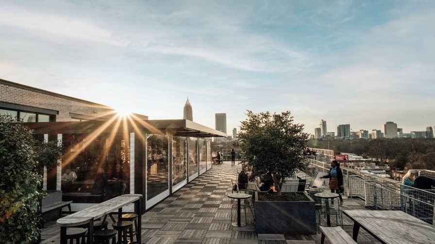 The outdoor dining are at 9 Mile Station with wooden tables and benches with the city behind it in Atlanta, Georgia, USA