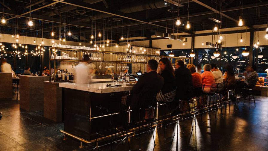 A dining room with a bar in the center full of people with singular light bulbs hanging from the ceiling at Bacchanalia in Atlanta, Georgia, USA